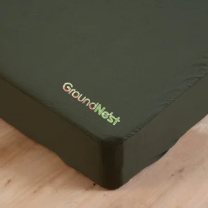 Del temno zelene prevleke iz blaga, izvezene z napisom GroundNest v beli in zeleni barvi, leži elegantno na lesenih tleh. Ta vrhunska ozemljitvena rjuha brezhibno združuje stil in funkcionalnost.